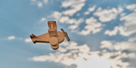 Wooden toy light aircraft biplane in the cloudy sky. Cartoon aviation.