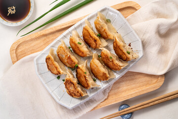 Pan-fried gyoza dumpling jiaozi in a plate with soy sauce on white table background.