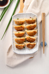 Pan-fried gyoza dumpling jiaozi in a plate with soy sauce on white table background.