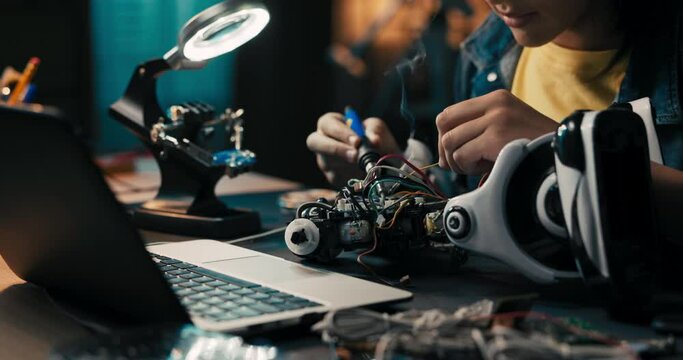 Close-up soldering, young teenager fixes cables,robot wires, small smoke rises from heated electronics, child spends leisure time on hobby.