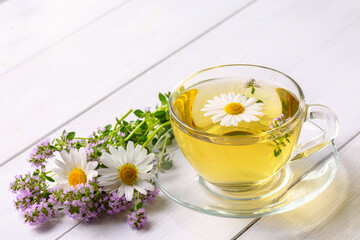 Herbal tea with chamomile and thyme in a transparent cup on a white wooden table