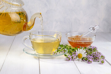 Herbal tea with chamomile and thyme in a transparent cup on a white wooden table
