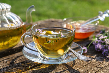 Herbal tea with chamomile and thyme in a transparent cup on an old wooden table on a sunny day