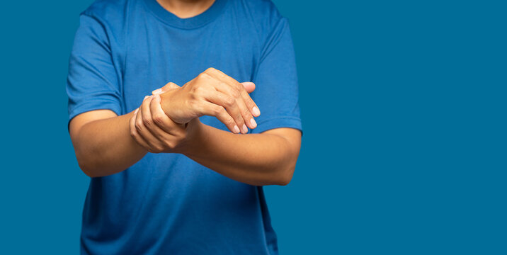 Close-up of hand female suffering from wrist pain while standing on a blue background