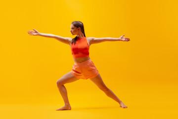 Fototapeta na wymiar Young beautiful slim, flexible girl in shorts doing stretching exercises isolated on bright yellow background. Sport, health, active lifestyle