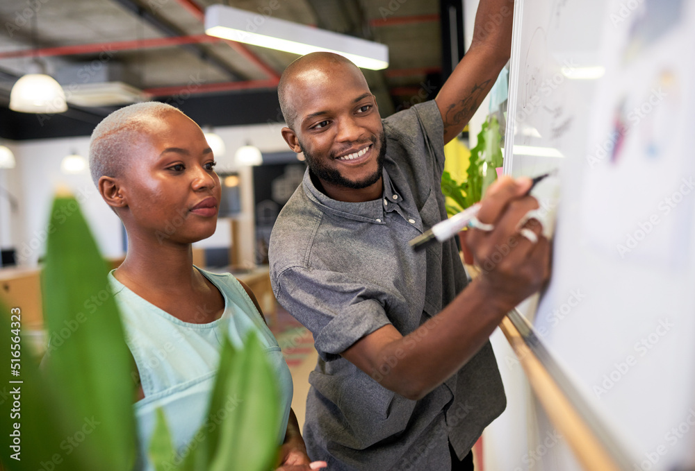 Wall mural a black man writes on a whiteboard while brainstorming with colleague in office