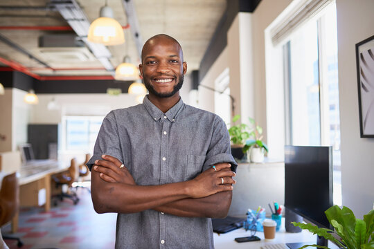 An attractive Black man stands with arms crossed in creative office workplace