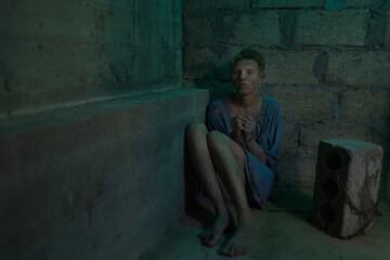 A young dirty man in tattered clothes is locked in a concrete basement