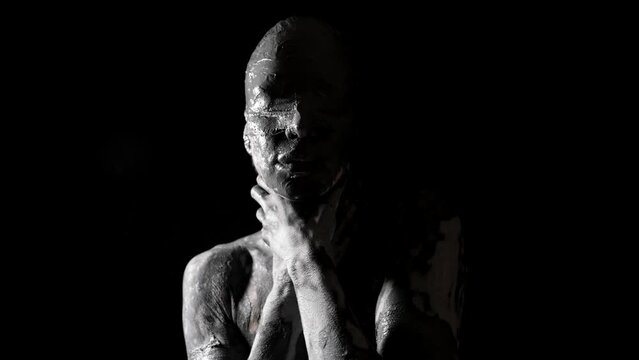 a portrait of a woman with blindfolded eyes and a face smeared with clay. she squeezes neck with hands. close-up. black and white video