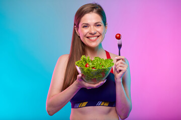 Sporty woman in sportswear green salad in glass bowl and red tomato on fork. Female fitness portrait isolated on neon multicolor background.