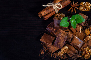 A pile of dark broken chocolate sprinkled with cocoa powder, nuts and spices. Copy space