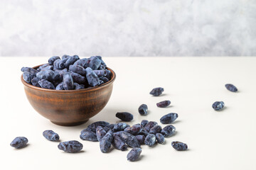 Honeyberry (Lonicera caerulea). Sweet honeysuckle berries in a clay bowl on a light background