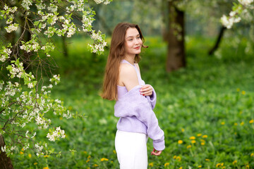 Naklejka na ściany i meble A young girl in a sweater next to white flowers on a tree