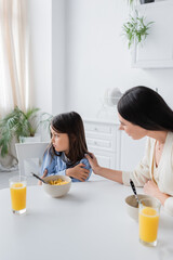 Obraz na płótnie Canvas nanny calming upset girl looking away near corn flakes and orange juice in kitchen.
