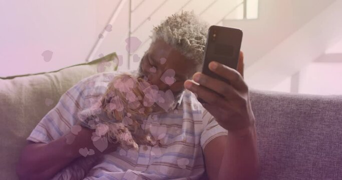 Animation of falling hearts over african american senior man using smartphone