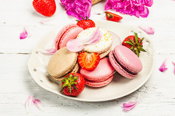 Macarons with strawberries and peonies flower petals, on a white wooden background
