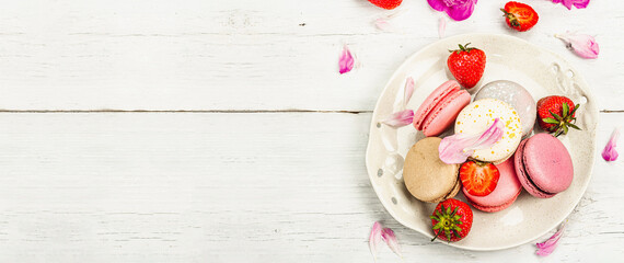 Obraz na płótnie Canvas Macarons with strawberries and peonies flower petals, on a white wooden background