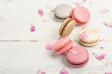 Macarons with peony flower petals on a white wooden background. Sweet dessert, pastel colors