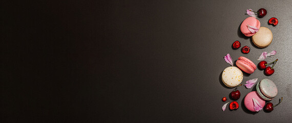 Macarons with peonies flower petals and ripe cherries on a black stone background. Sweet dessert