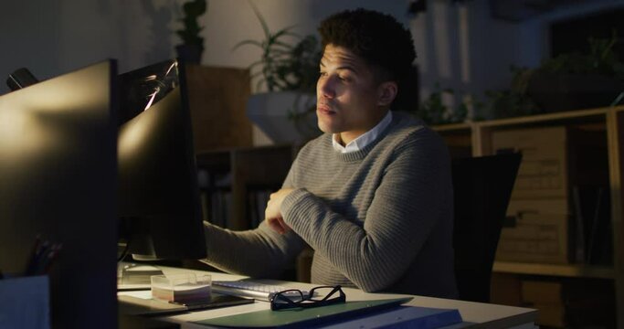 Video of tired biracial man with coffee using computer, working late in office