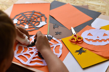 Close-up of children's hands that create paper crafts for Halloween. Homemade decorations for the holiday.
