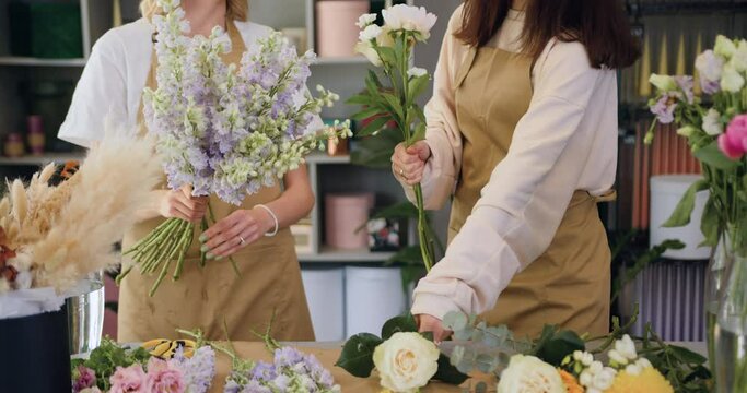 Two female florist workers working in flower shop. Good-looking young girls making bouquet of roses and dried flowers at workplace.