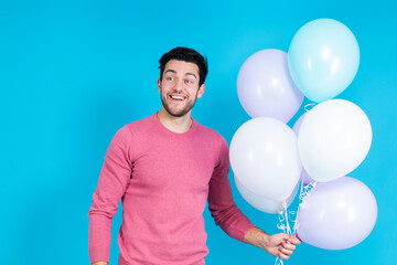 Smiling Happy Caucasian Guy Handsome Brunet Man With Bunch of Colorful Air Balloons in Pink Jumper Standing On Blue Background.