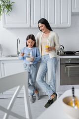 full length of girl eating corn flakes near nanny with fresh orange juice.