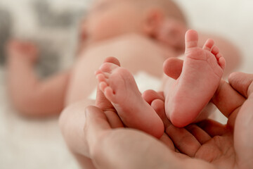 Obraz na płótnie Canvas Men's hands hold the small legs of a newborn baby