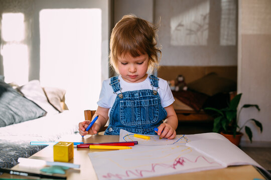 Small child at home at the children's table draws with felt-tip pens.