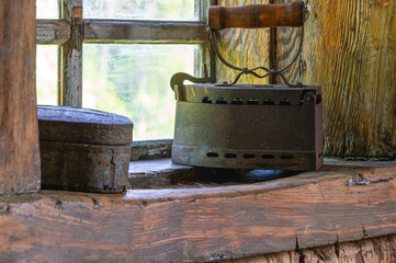 An old cast-iron coal iron made in the 19th century on the windowsill of an old wooden house. The interior of an old house. Dark log walls of the house. Rustic architecture.
