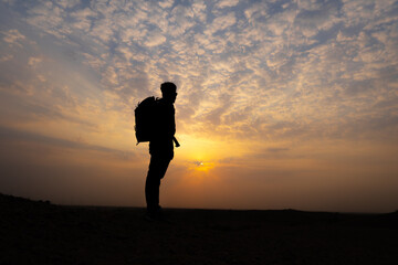 Silhouette shot of an Indian hiker staring at the sun during the sunset. Man looks at the beautiful sunset from above the hill. Natural background