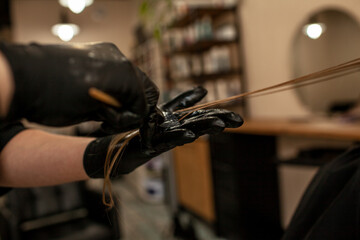 
Close-up of female hands holding the hair rows in professional hairstyles salon. The hairdresser paints or makes keratin to a girl in a professional salon