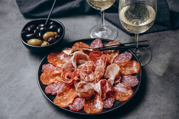 Salami on a black plate and olives and r white wine or Prosecco in a restaurant aperitif meal