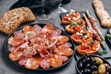 Food antipasto prosciutto ham, salami, olives and  bread sticks. cheese on a board parmesan, pecorino, gorgonzola. Tomato and basil bruschetta. Two glasses of white wine or Prosecco