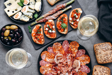 Food antipasto prosciutto ham, salami, olives and  bread sticks. cheese on a board parmesan, pecorino, gorgonzola. Tomato and basil bruschetta. Two glasses of white wine or Prosecco