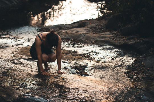 Young Colombian woman making meditation in a river (and praying Pachamama) with her hands and feet in the fresh water. Villeta, Cundinamarca, Colombia.