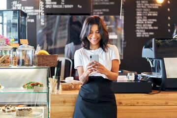 Portrait of smiling waitress barista using mobile phone at work - obrazy, fototapety, plakaty