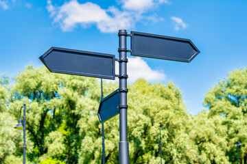 Blank signs with directions in the park. Black arrows against the sky and green trees.