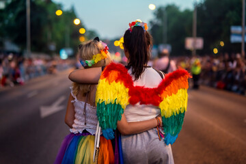 Two girls cuddled up with rainbow wings at Pride 2022