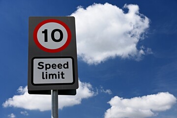 UK road sign 10 mph speed limit against a blue cloudy sky.