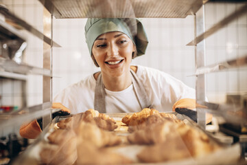 Female baker at the kitchen holding freshly baked croiisants
