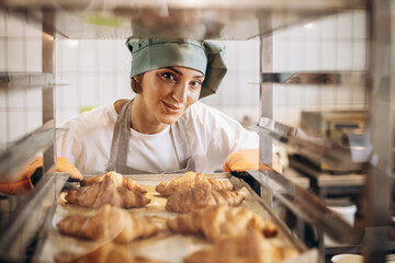 Female baker at the kitchen holding freshly baked croiisants - obrazy, fototapety, plakaty