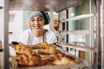 Female baker at the kitchen holding croissant - Powered by Adobe