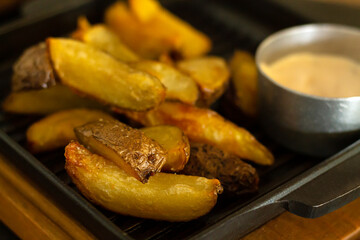 Fried potato wedges pan with sauce closeup