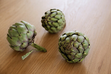 Obraz premium Fresh green Italian Artichoke natural wood background. Organic local produce vegetable on textured table. Vegan diet. Clean eating concept. Close up, top view, flat lay.