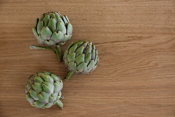 Fototapeta premium Fresh green Italian Artichoke natural wood background. Organic local produce vegetable on textured table. Vegan diet. Clean eating concept. Close up, top view, flat lay.