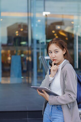 Portrait of an Asian schoolgirl Smiling looking at the camera holding a tablet standing in front of the building.