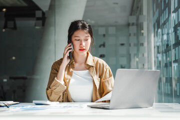 Young Asian business female freelancer talking on smartphone at workspace, to get job done.