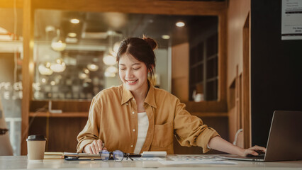 Smiling asian business woman using laptop to get job done sitting in a modern office.